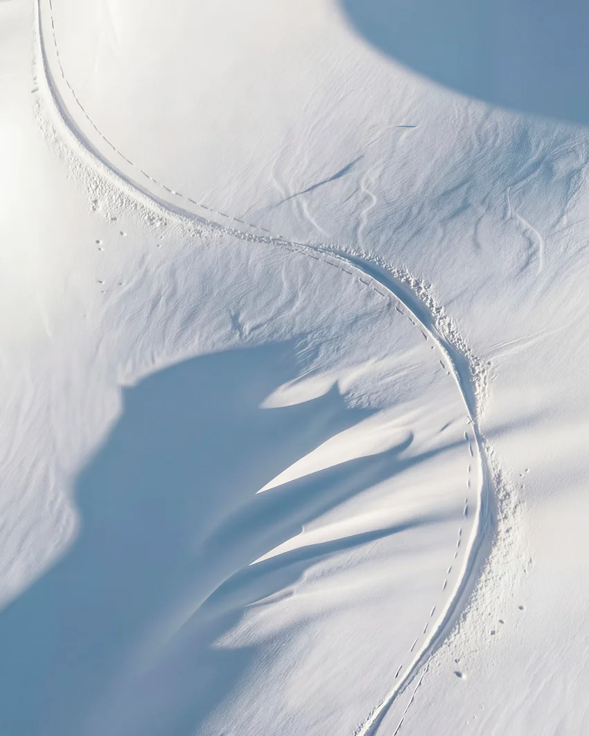 Aerial view of wind-sculpted snow ridges and ski tracks curving across an alpine slope for Dom Pérignon — 3d product visualization Thinkdiff, photography & art direction by Pierrick Jégou, produced by Thinkdiff AI Production House