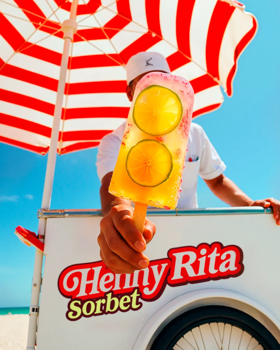 Man holding two cocktail glasses beside a red and white striped umbrella and a "Henny Rita Sorbet" cart — virtual production studio Thinkdiff, photography & art direction by Thinkdiff AI Production House