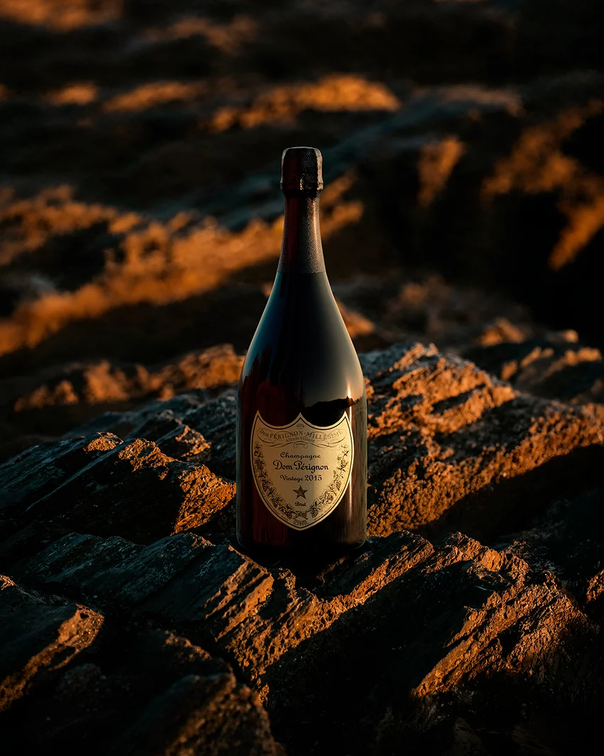Dom Pérignon bottle standing on sunlit rocks at golden hour with the sea stretching behind — virtual production studio Thinkdiff, photography & art direction by Pierrick Jégou, produced by Thinkdiff AI Production House