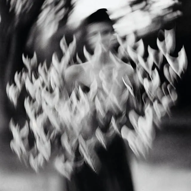 Black and white motion-blurred figure surrounded by scattering leaves or feathers, dynamic double-exposure effect — luxury video production Thinkdiff, generative AI artwork & art direction by Charlie Faye Mather