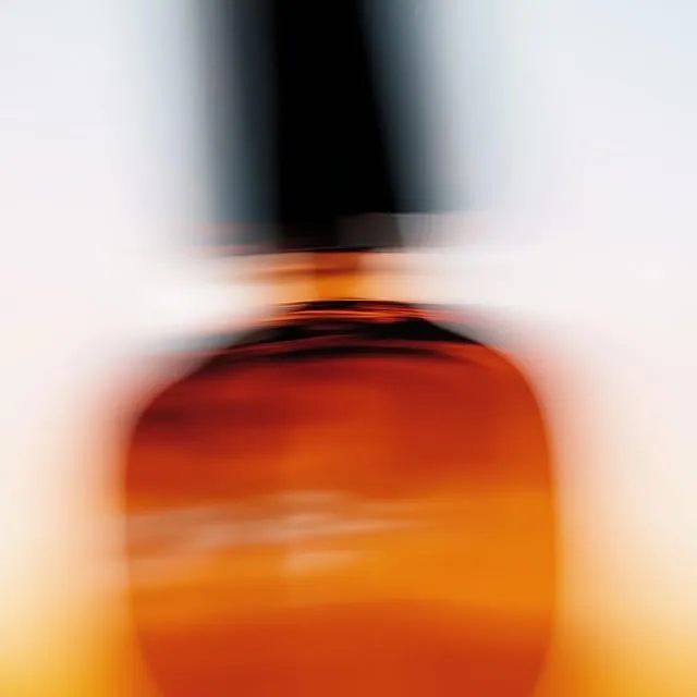 Motion-blurred amber glass perfume bottle with a dark cap, warm orange tones streaking across the frame — ai video production Thinkdiff, generative AI artwork & art direction by Charlie Faye Mather