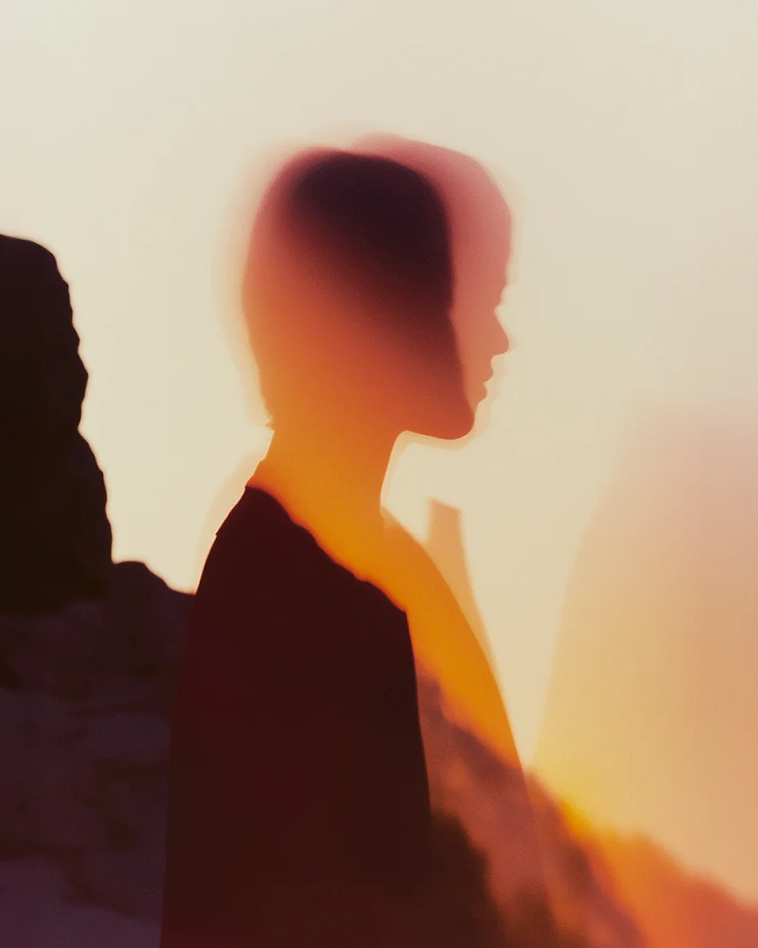 Soft-focus profile silhouette of a woman bathed in warm golden light beside dark rock formations — ai advertising agency Thinkdiff, photography & art direction by Pierrick Jégou, produced by Thinkdiff AI Production House