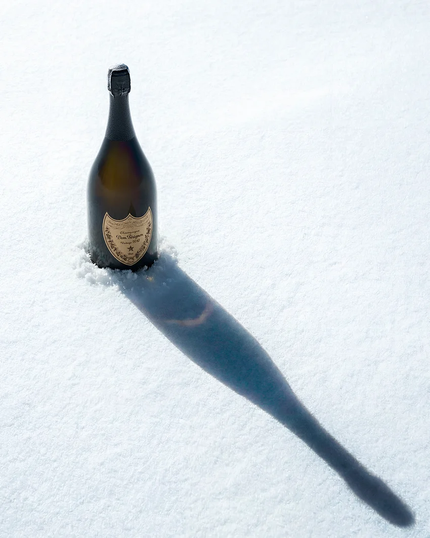 Dom Pérignon bottle standing upright in fresh snow, casting a long diagonal shadow under bright sunlight — 3d product animation Thinkdiff, photography & art direction by Pierrick Jégou, produced by Thinkdiff AI Production House