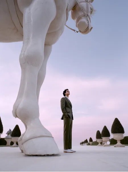 Woman standing beside the towering legs of a white horse statue in a pastel-toned garden setting — cgi studio Thinkdiff, photography & art direction by Alex, produced by Thinkdiff AI Production House
